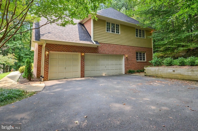 view of front of property featuring a garage, driveway, brick siding, and roof with shingles