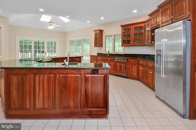 kitchen featuring high quality fridge, a skylight, dishwasher, an island with sink, and glass insert cabinets