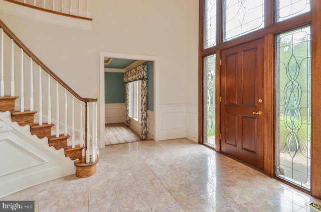 entryway with a wainscoted wall, stairway, a towering ceiling, and a decorative wall