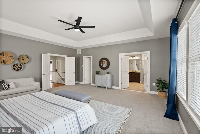 carpeted bedroom featuring a raised ceiling, connected bathroom, ceiling fan, and multiple windows