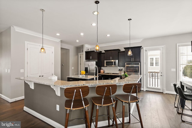 kitchen with hanging light fixtures, stainless steel appliances, a large island with sink, a kitchen bar, and decorative backsplash