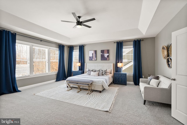 carpeted bedroom featuring a raised ceiling, multiple windows, and ceiling fan