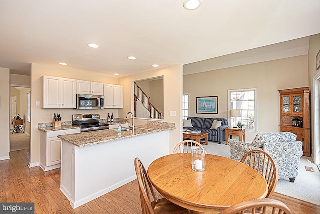 kitchen featuring appliances with stainless steel finishes, sink, white cabinetry, light stone counters, and light hardwood / wood-style floors