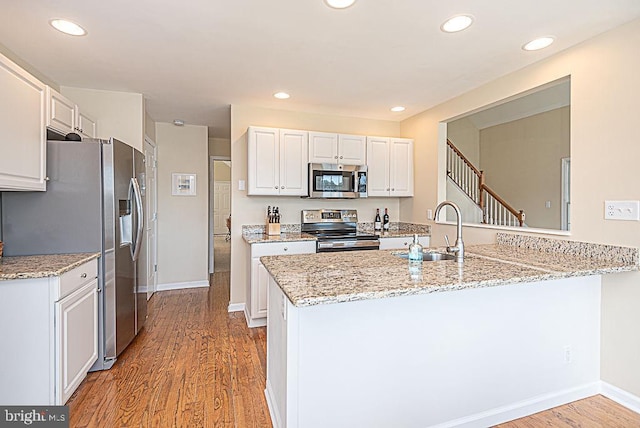 kitchen featuring white cabinetry, sink, kitchen peninsula, stainless steel appliances, and light stone counters