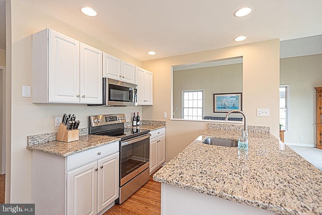 kitchen with kitchen peninsula, sink, white cabinets, light stone counters, and stainless steel appliances