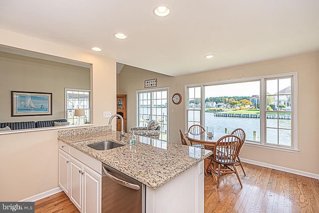 kitchen with stainless steel dishwasher, sink, white cabinets, a water view, and light stone counters