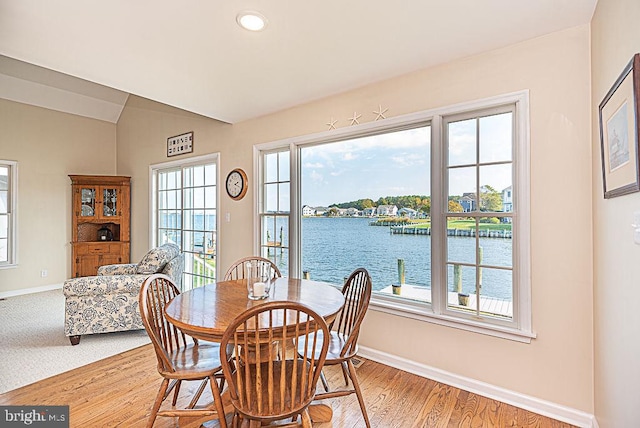 dining space with wood-type flooring, a water view, and vaulted ceiling