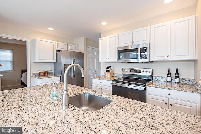 kitchen with sink, stainless steel appliances, white cabinetry, and light stone counters