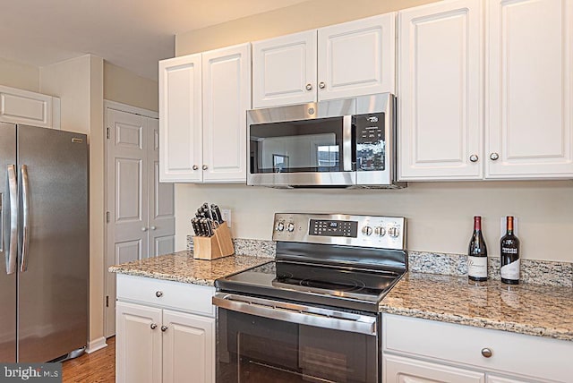 kitchen featuring wood-type flooring, light stone counters, white cabinetry, and appliances with stainless steel finishes