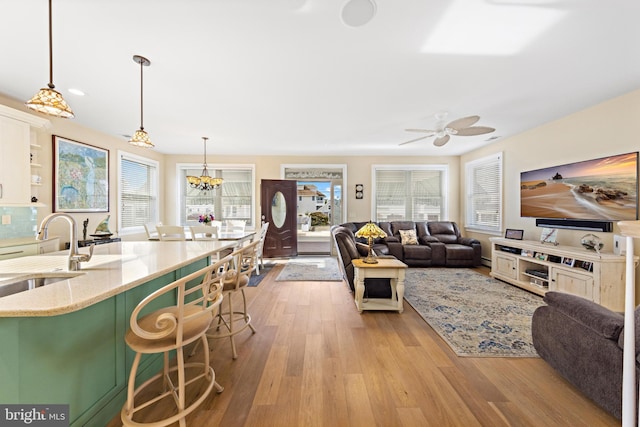 living room featuring ceiling fan with notable chandelier, light hardwood / wood-style floors, and sink