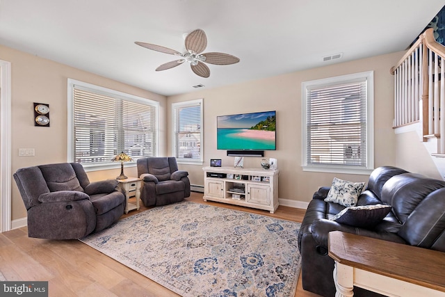 living room with light hardwood / wood-style floors, baseboard heating, ceiling fan, and a healthy amount of sunlight