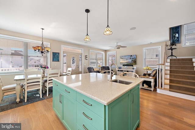 kitchen featuring sink, hanging light fixtures, an island with sink, ceiling fan with notable chandelier, and green cabinetry