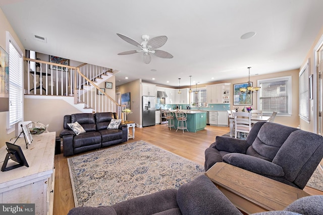 living room with ceiling fan with notable chandelier and light wood-type flooring