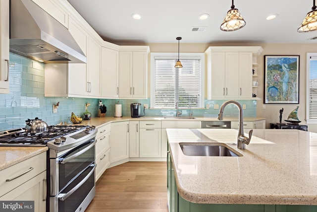 kitchen with stainless steel range with gas stovetop, light stone counters, hanging light fixtures, and wall chimney range hood