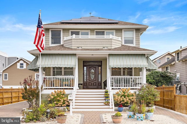 view of front of home featuring covered porch, solar panels, and a balcony