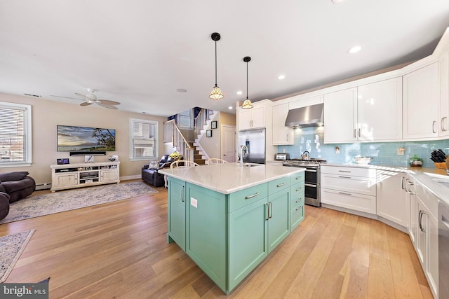 kitchen with a center island, white cabinets, stainless steel appliances, and wall chimney range hood