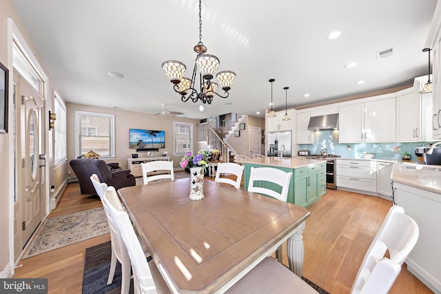 dining area with baseboard heating, sink, ceiling fan with notable chandelier, and light wood-type flooring