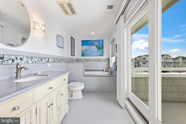 bathroom featuring tile patterned floors, a tub to relax in, toilet, vanity, and tile walls