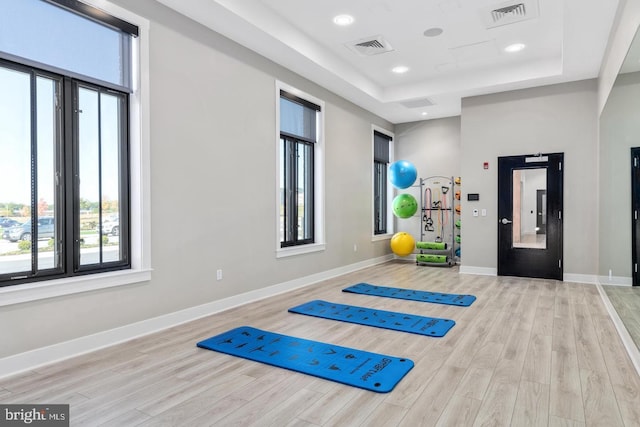 workout area featuring a raised ceiling and light wood-type flooring