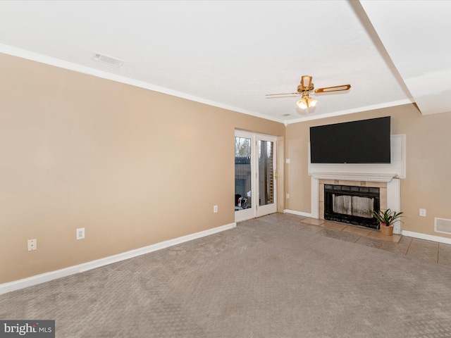 unfurnished living room with a tiled fireplace, ceiling fan, light colored carpet, and ornamental molding