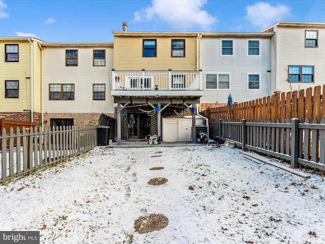 snow covered rear of property with a shed and a wooden deck