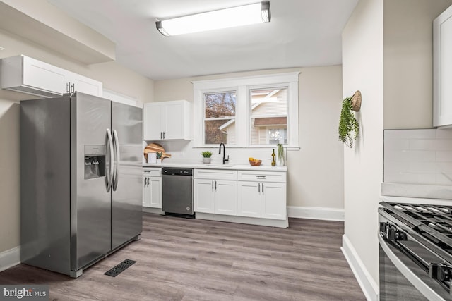 kitchen featuring decorative backsplash, appliances with stainless steel finishes, light wood-type flooring, sink, and white cabinetry