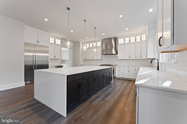 kitchen with stainless steel appliances, a spacious island, wall chimney range hood, white cabinetry, and hanging light fixtures