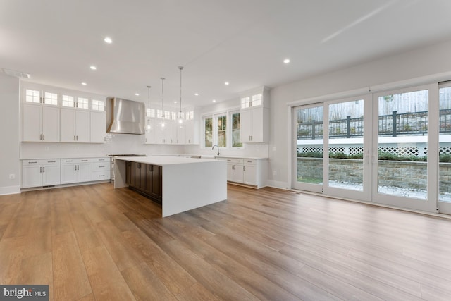 kitchen featuring a kitchen island, wall chimney range hood, hanging light fixtures, and white cabinetry