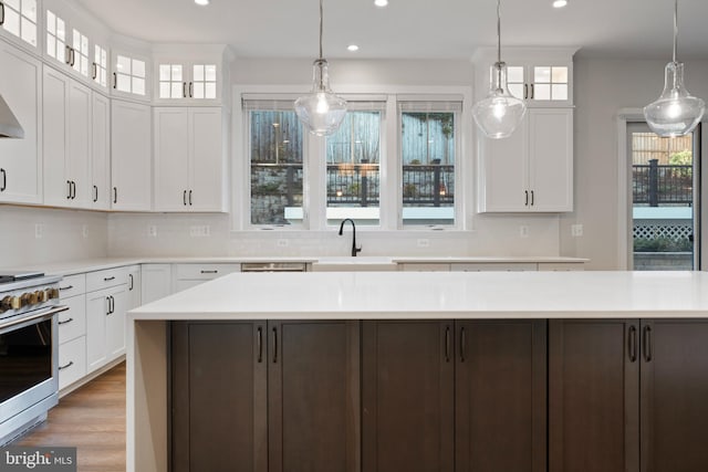 kitchen with pendant lighting, sink, stainless steel stove, a kitchen island, and white cabinetry