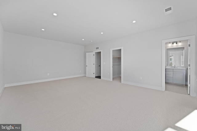 unfurnished bedroom with light carpet, a walk in closet, sink, connected bathroom, and a closet