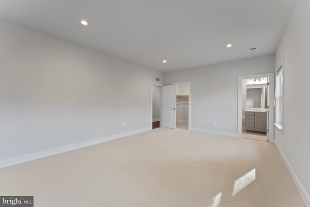 unfurnished bedroom with ensuite bathroom, light colored carpet, and a spacious closet