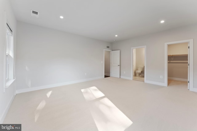 unfurnished bedroom with connected bathroom, light colored carpet, a spacious closet, and a closet