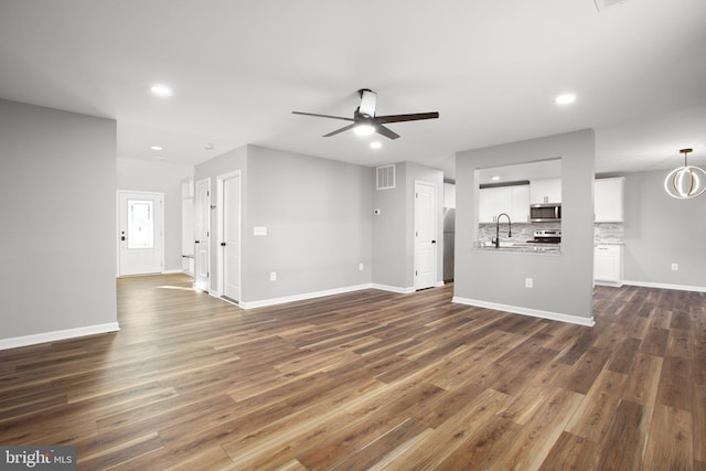 unfurnished living room featuring ceiling fan with notable chandelier, sink, and dark wood-type flooring