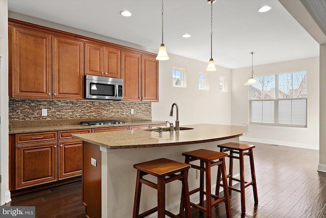 kitchen with appliances with stainless steel finishes, decorative light fixtures, a kitchen island with sink, and sink