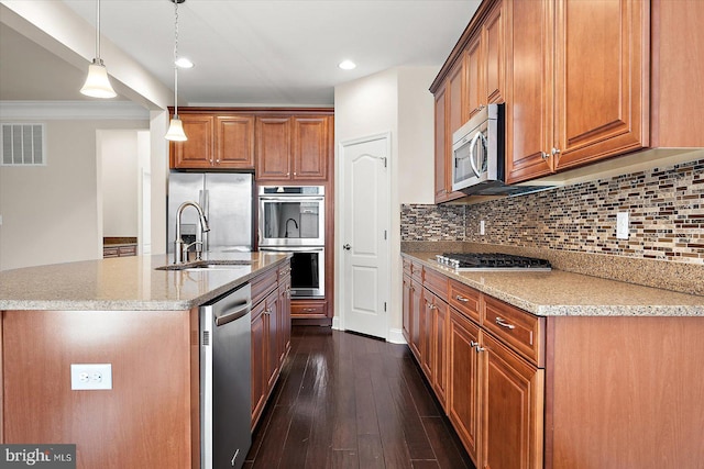 kitchen featuring decorative backsplash, stainless steel appliances, a kitchen island with sink, sink, and hanging light fixtures