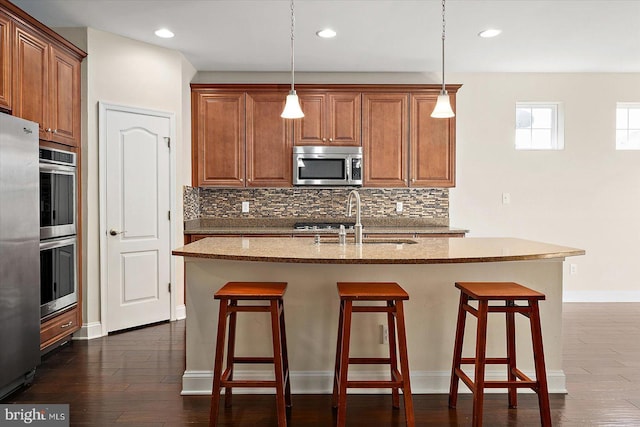 kitchen with sink, an island with sink, pendant lighting, and appliances with stainless steel finishes