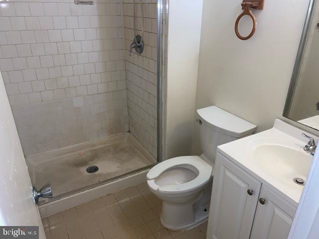 bathroom featuring toilet, a tile shower, vanity, and tile patterned floors