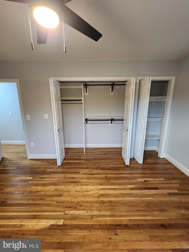 unfurnished bedroom featuring hardwood / wood-style flooring, ceiling fan, and multiple closets