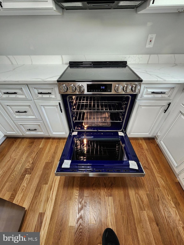 interior details featuring light hardwood / wood-style flooring, white cabinetry, stainless steel electric stove, and light stone counters