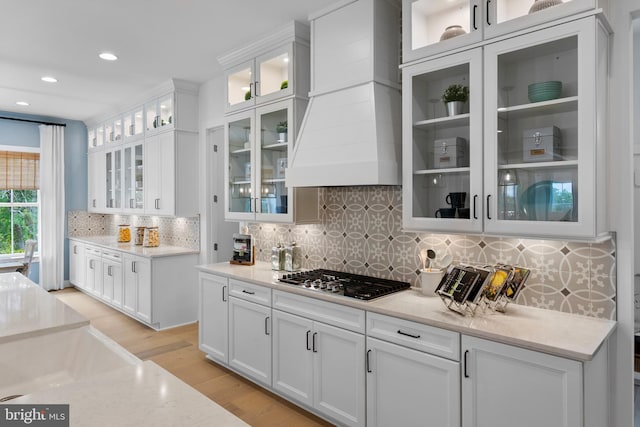 kitchen with premium range hood, white cabinetry, light stone counters, and stainless steel gas cooktop