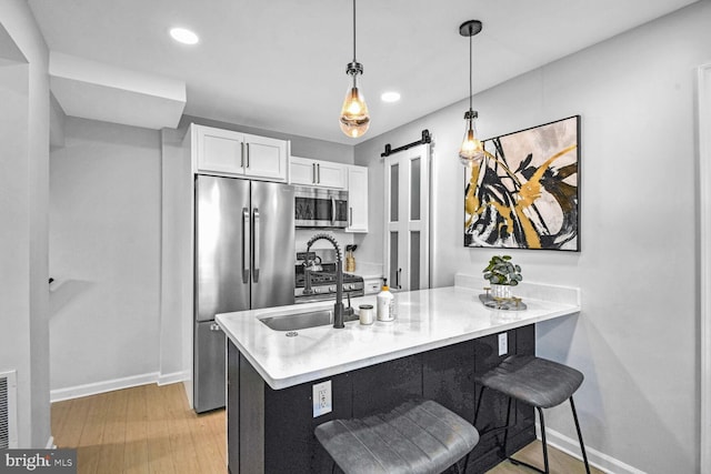 kitchen featuring a breakfast bar, appliances with stainless steel finishes, white cabinetry, kitchen peninsula, and a barn door