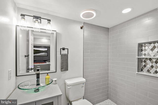 bathroom with vanity, tiled shower, and toilet