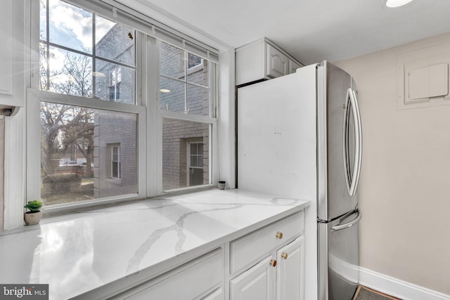 kitchen with light stone countertops, stainless steel fridge, and white cabinets