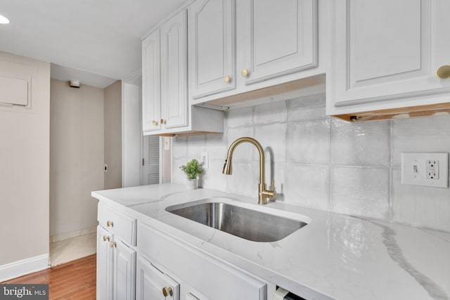 kitchen with white cabinets, sink, tasteful backsplash, light stone counters, and wood-type flooring