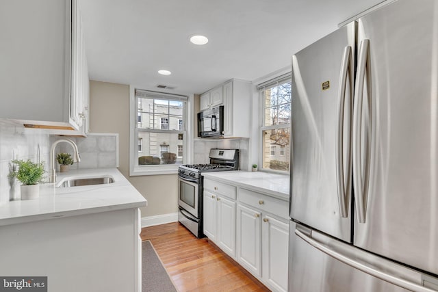 kitchen with plenty of natural light, white cabinetry, sink, and appliances with stainless steel finishes