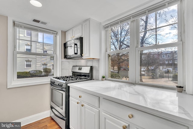 kitchen with white cabinetry, gas range, a wealth of natural light, and light stone counters