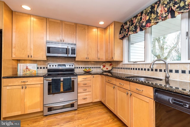 kitchen with appliances with stainless steel finishes, tasteful backsplash, dark stone counters, sink, and light hardwood / wood-style floors