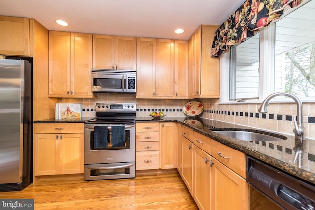 kitchen with dark stone countertops, sink, stainless steel appliances, and light brown cabinetry