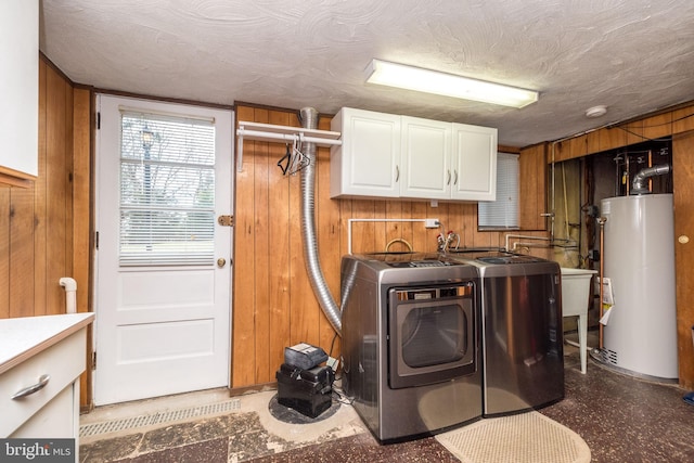 laundry area featuring cabinets, wooden walls, gas water heater, and washing machine and dryer