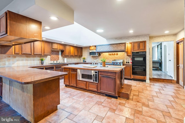 kitchen featuring backsplash, a center island with sink, kitchen peninsula, and black double oven